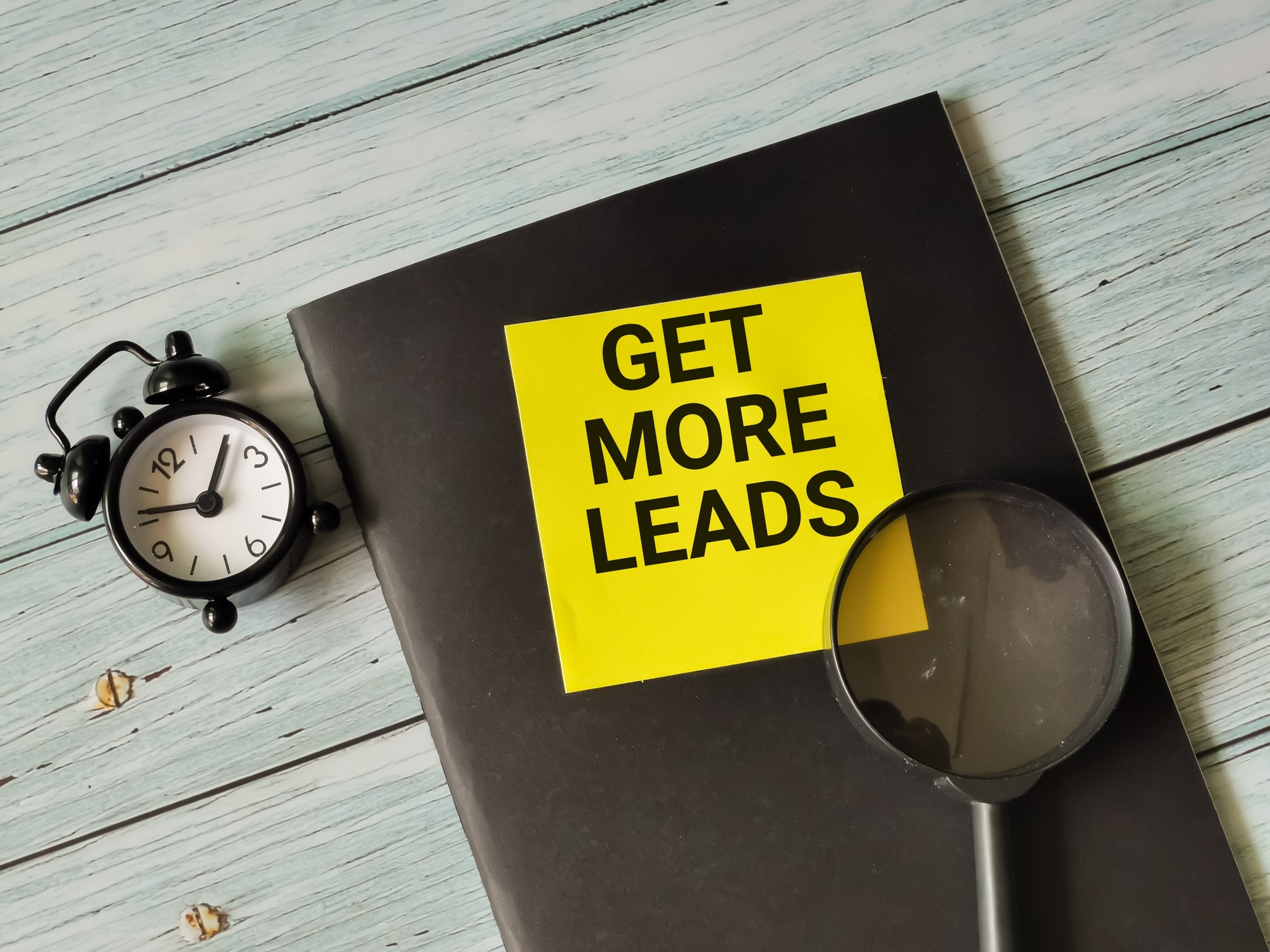 Phrase get more leads written on sticky note with alarm clock,magnifying glass and book for real estate agents lead generation strategies