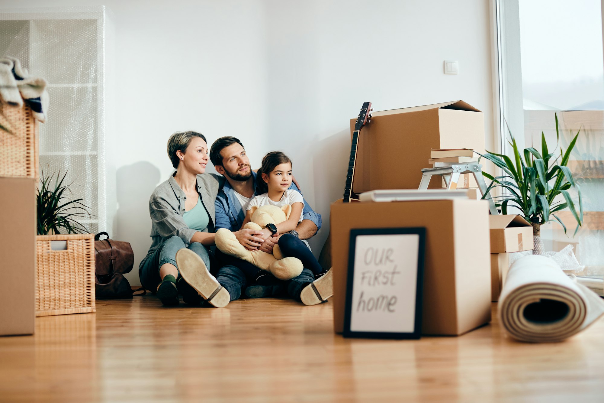 Parents buying a house with kids and relaxing on floor in their new living room.